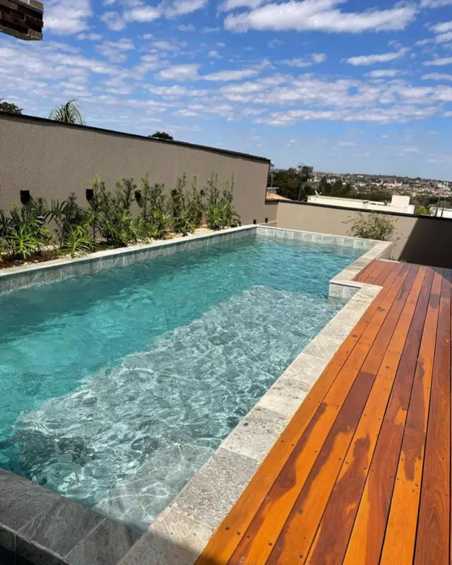 Piscina com borda de pedra clara e deck de madeira